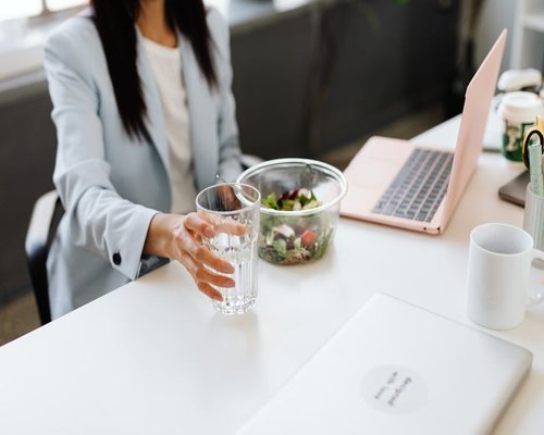 A person drinking water from a glass bottle at an office desk
